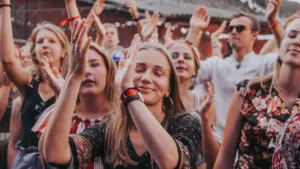 Noor naine naeratab kinnisilmi vabaõhukontserdil, ümbritsetud käsi tõstnud ja rõõmsatest noortest festivalikülastajatest.