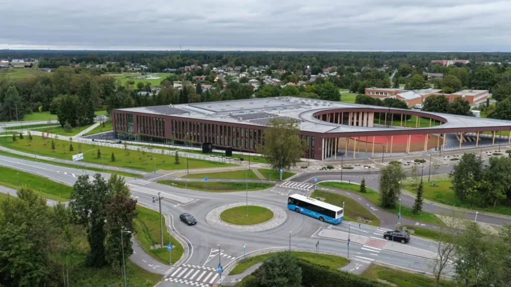Droonivaade tänapäevasest pruunist spordihoonest, mille kõrval asub bussiga ringristmik ja roheline elamurajoon.